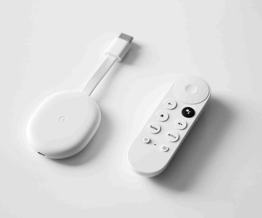 White Chromecast with Google TV device and voice remote on a light gray surface